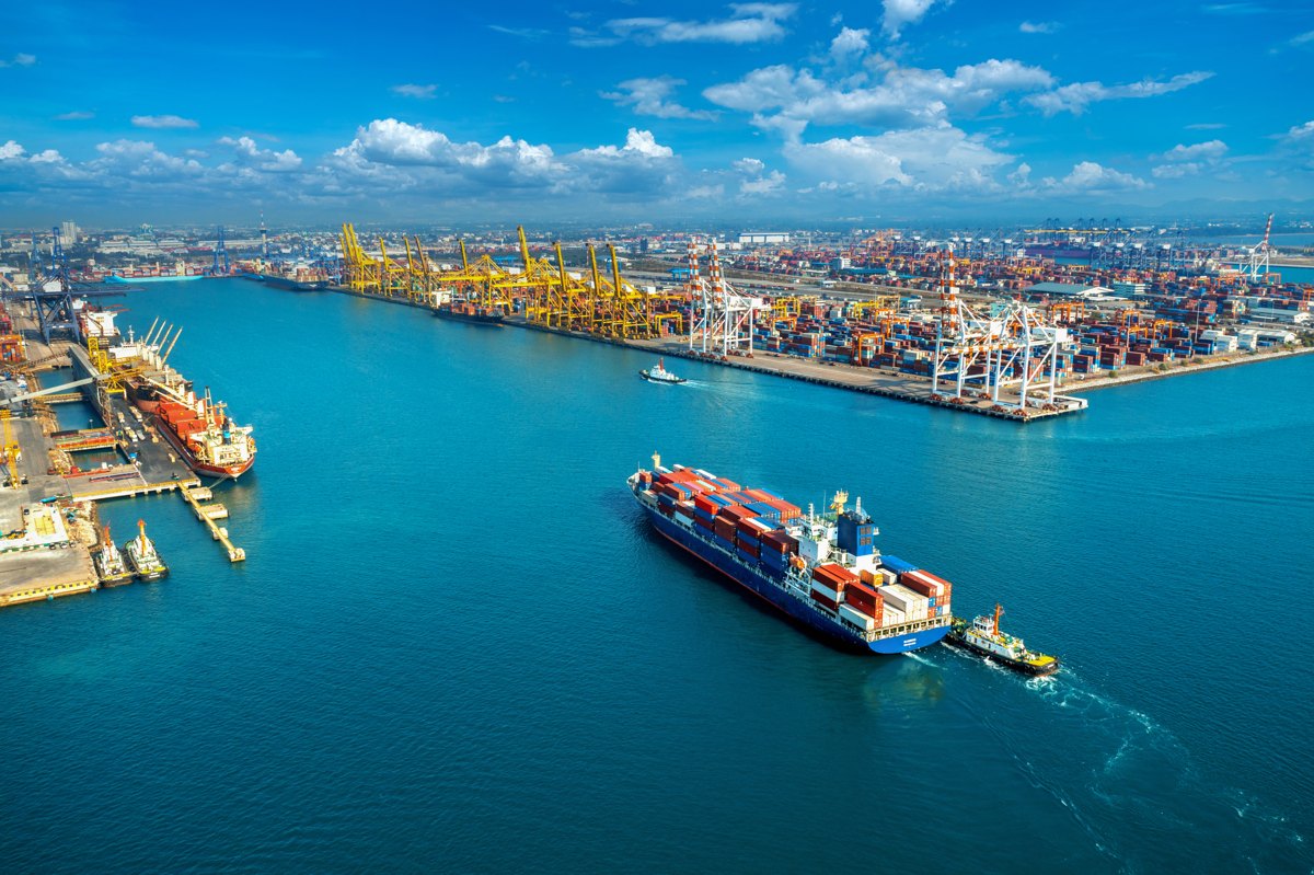 Container vessel beside stacked containers at a cargo terminal.