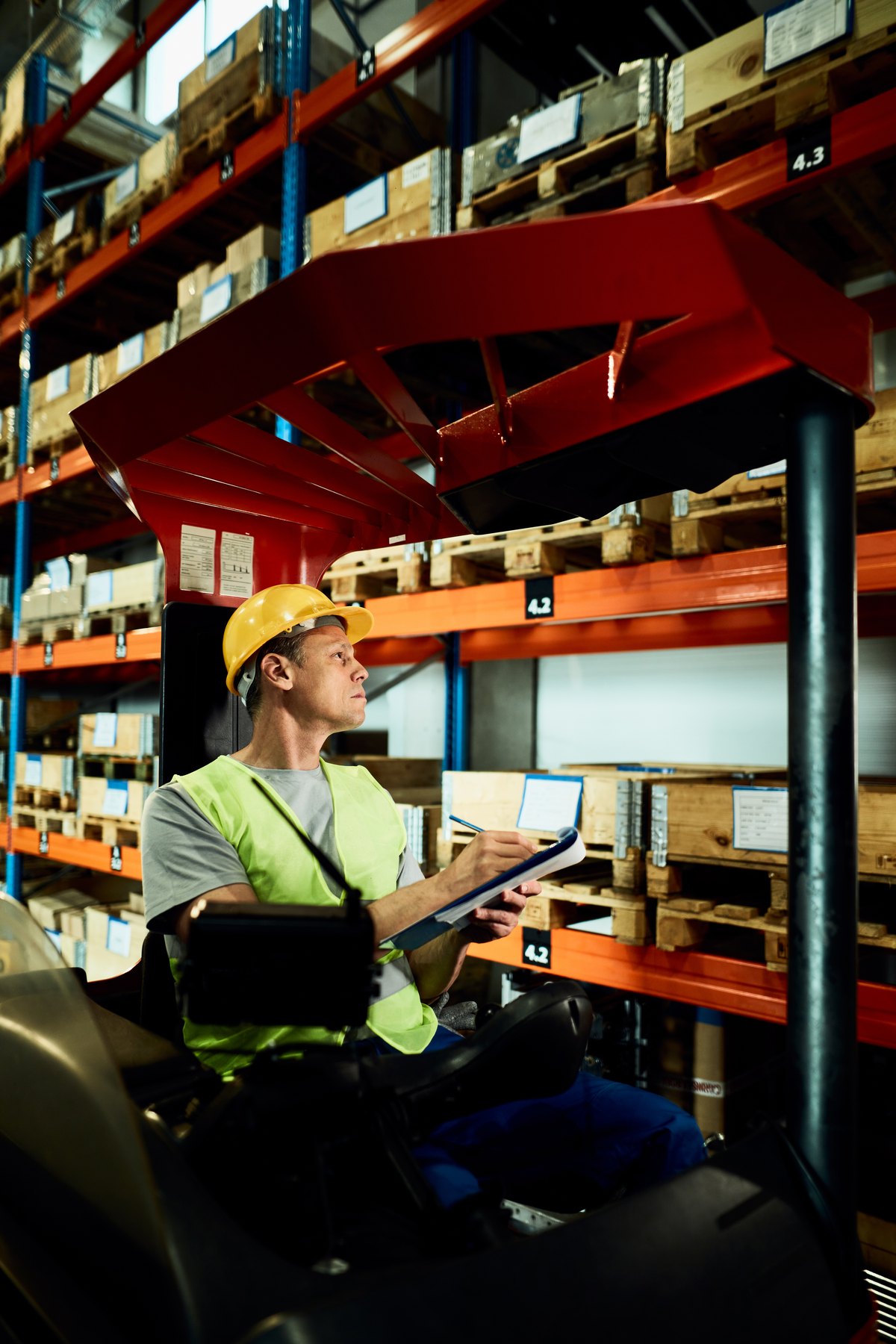 Forklift operator taking notes while examining stock of packages in a warehouse