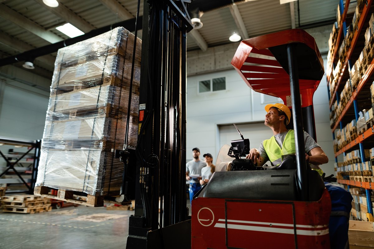 Forklift operator loading cargo while working in a warehouse his colleagues aree background