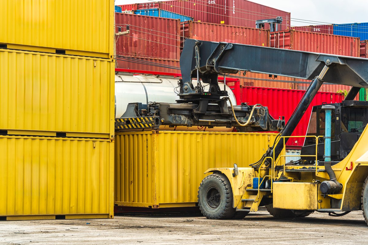 Container handler forklift moving cargo container in crowded shipping yard at port terminal