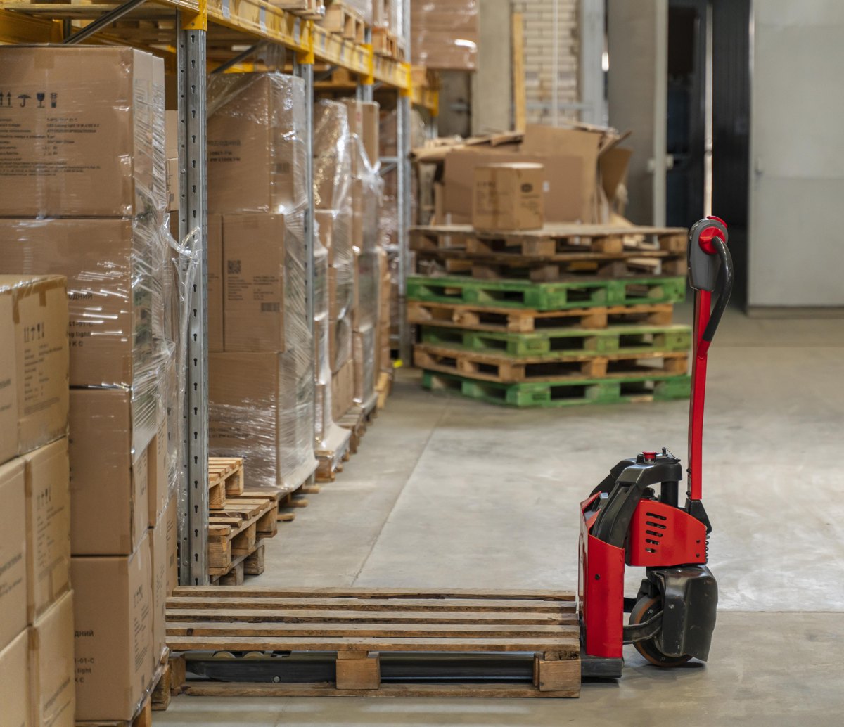 Manual pallet jack beside stacked wooden pallets in a warehouse.